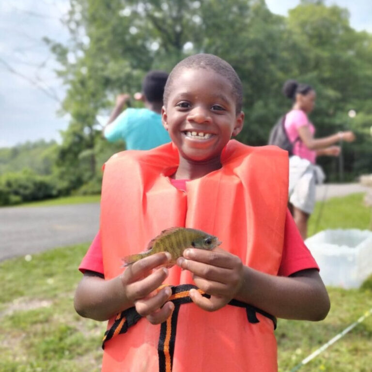 Smiling boy in orange life vest holding a small fish