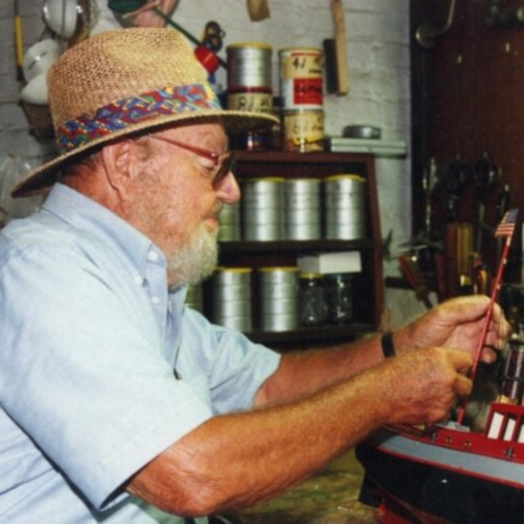 Elderly man building a model boat in workshop
