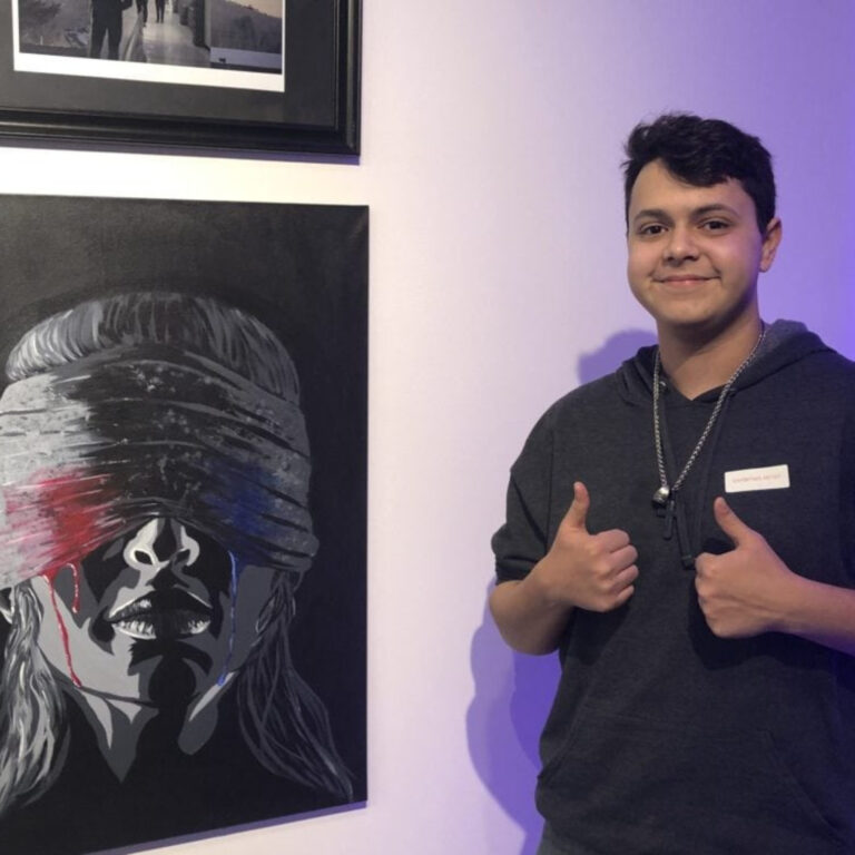 Young artist giving thumbs up beside his dramatic artwork