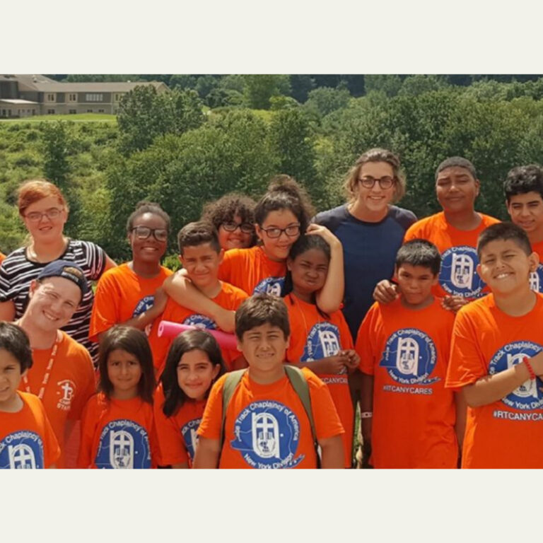 Children and adults in orange Race Track Chaplaincy shirts outdoors