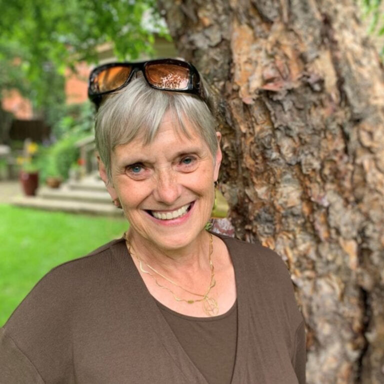 Smiling older woman with sunglasses on head near tree