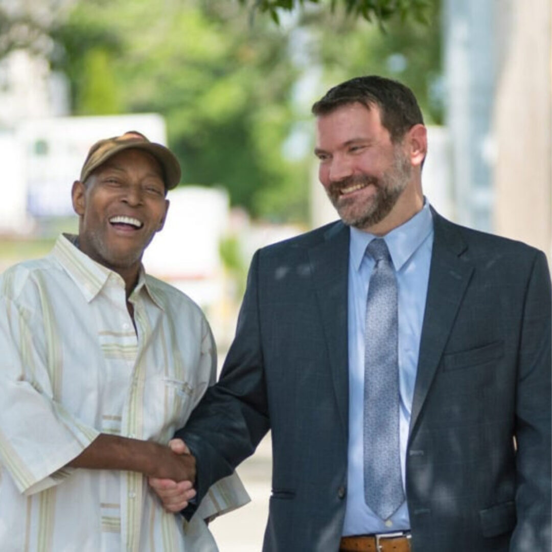 Two men shaking hands and smiling outdoors