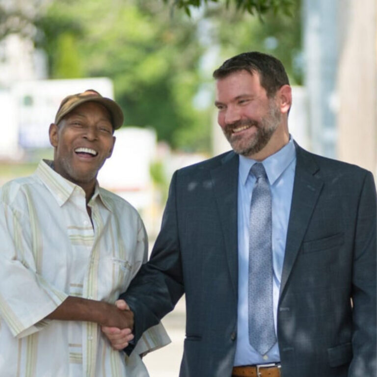 Two men shaking hands and smiling outdoors