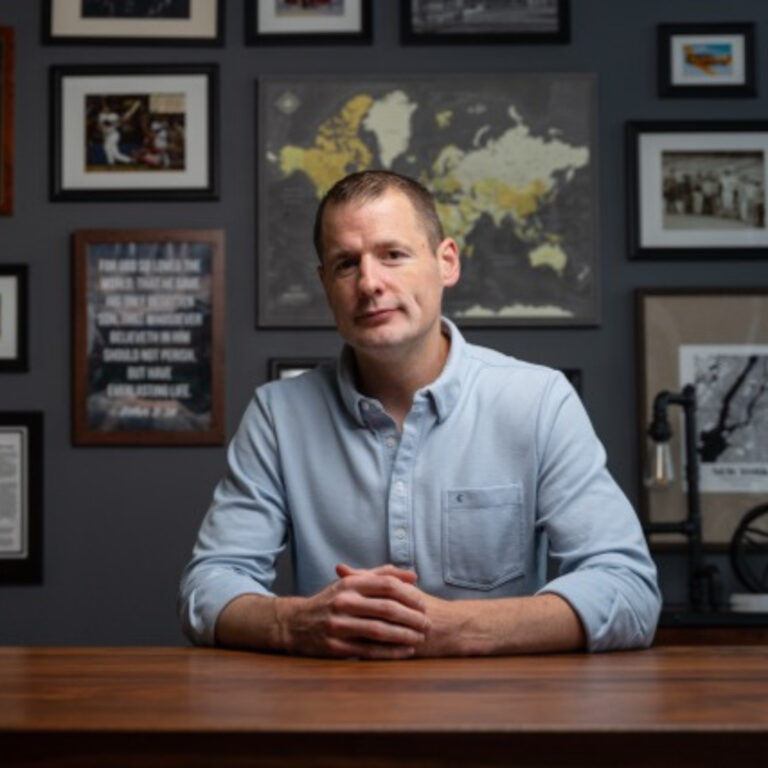 Man in blue shirt sitting at desk with gallery wall
