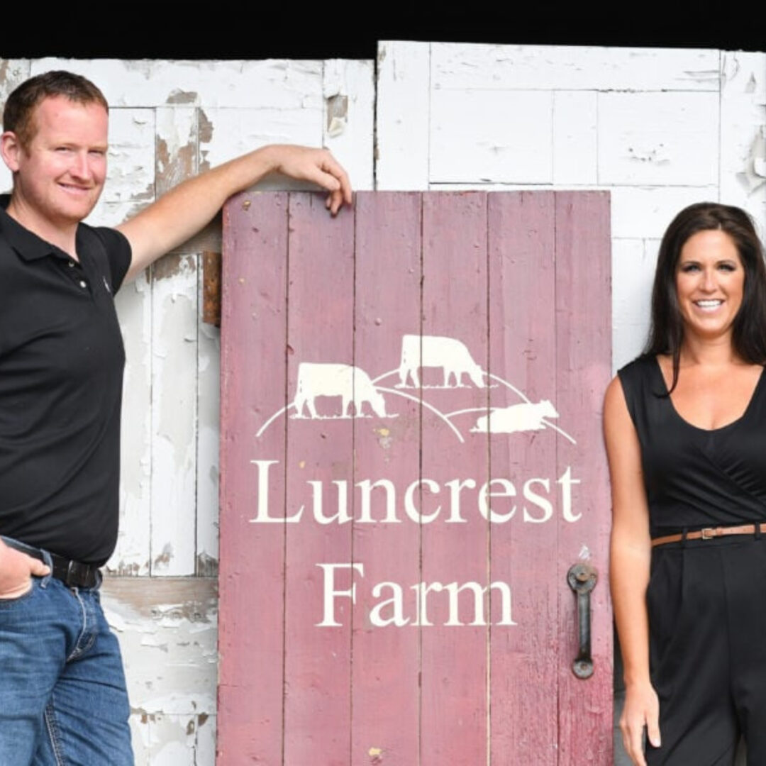 Man and woman posing with Luncrest Farm wooden sign