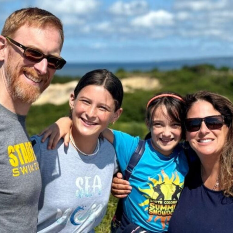 Happy family of four smiling outdoors near coastal dunes