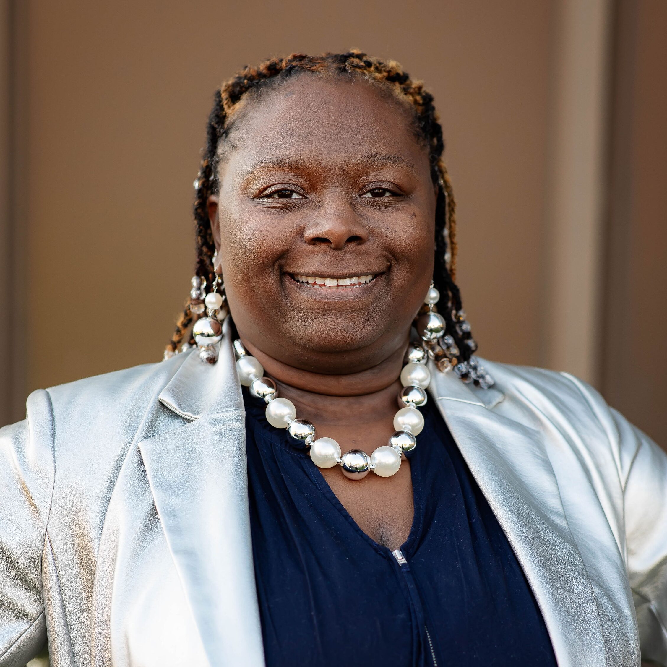 Person smiling wearing silver jacket and beaded necklace