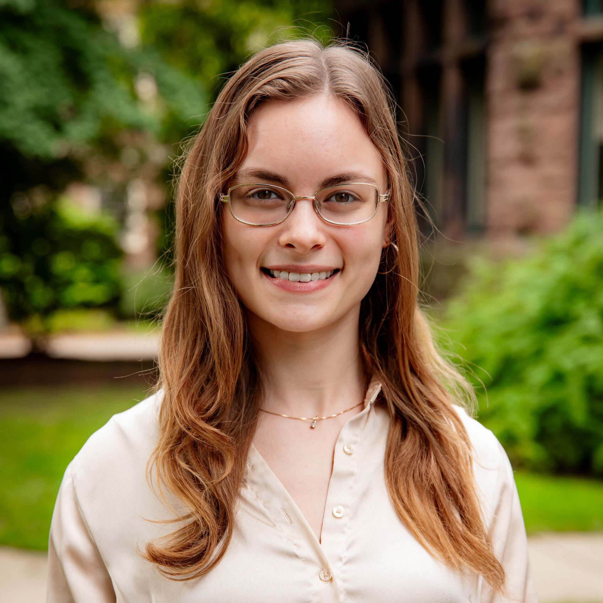 Young woman with glasses smiling outdoors near brick building