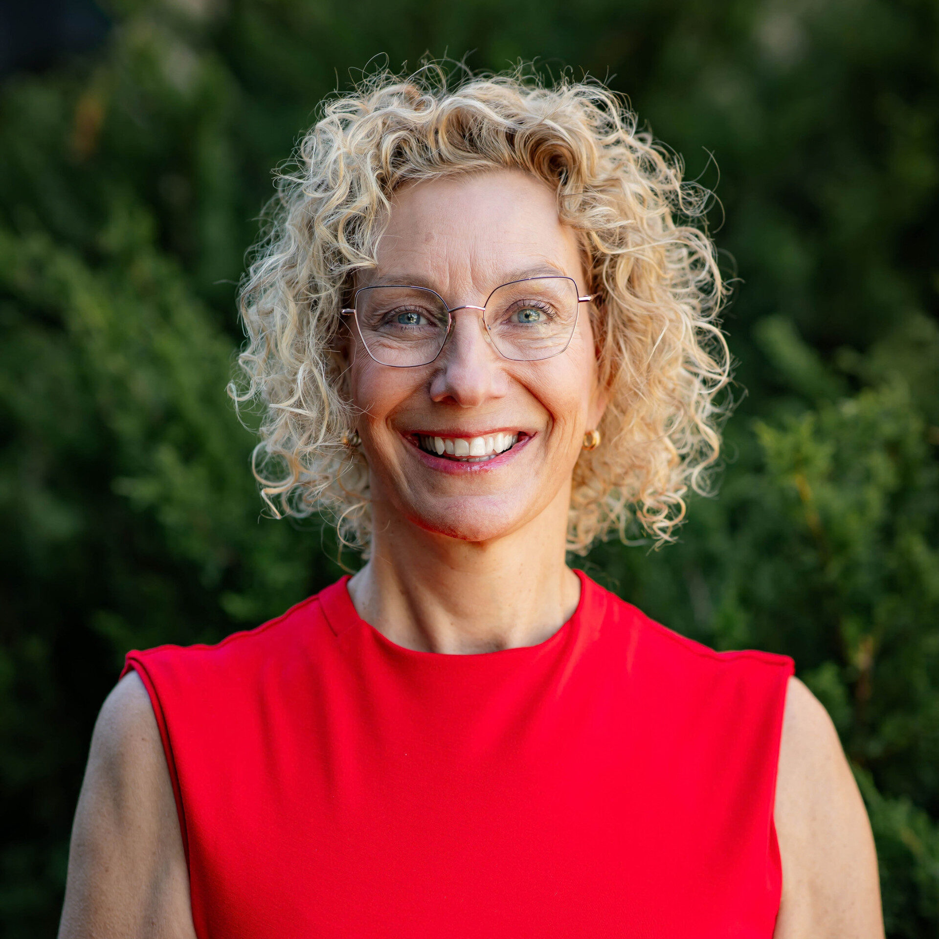 Smiling woman with curly blonde hair and glasses outdoors