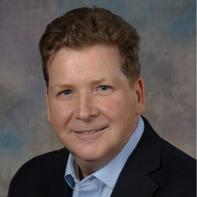 Professional headshot of smiling middle-aged man in blazer