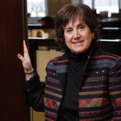 Smiling woman in colorful blazer leaning against doorframe
